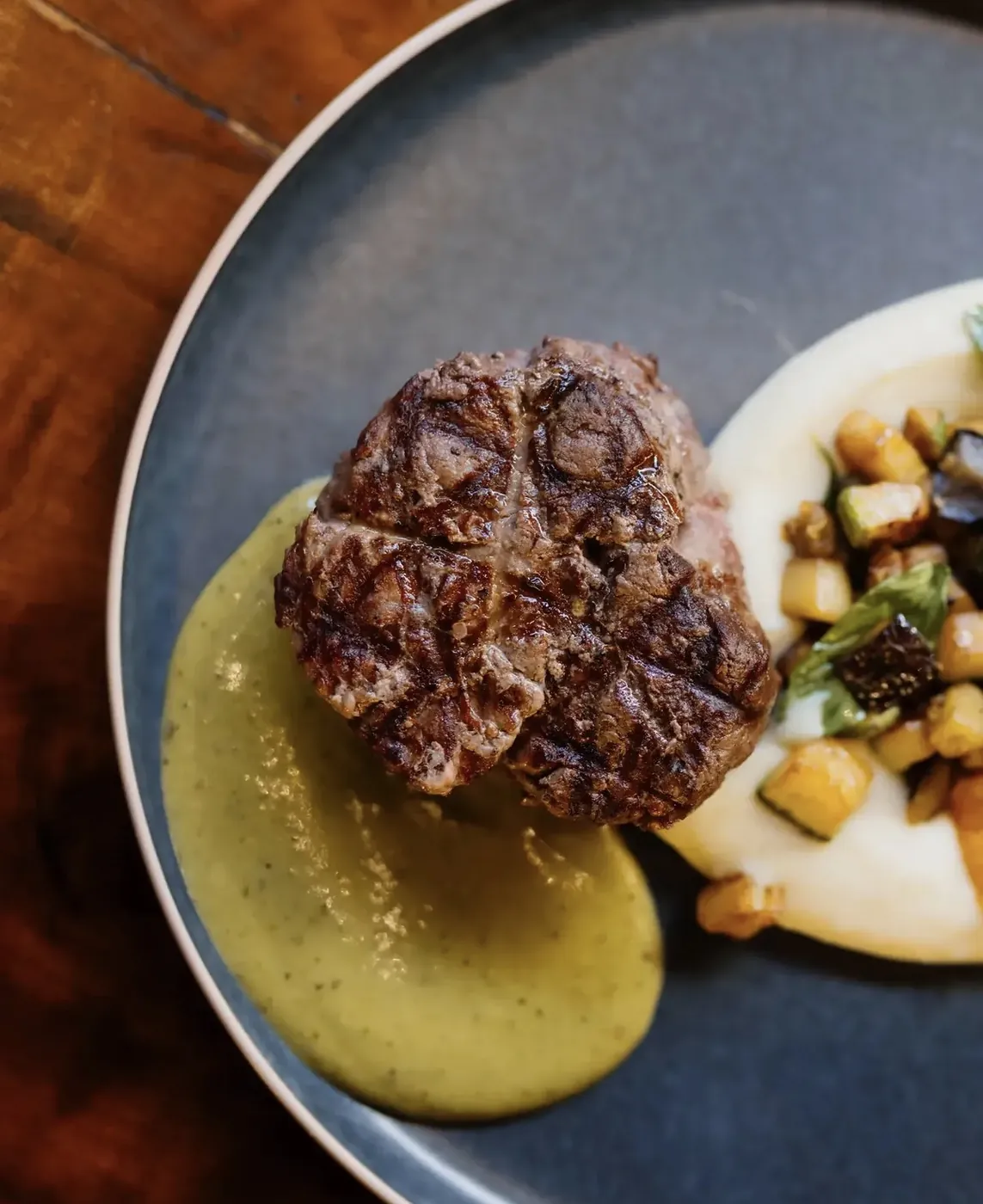 Medallón de res con salsa verde y vegetales salteados en plato azul